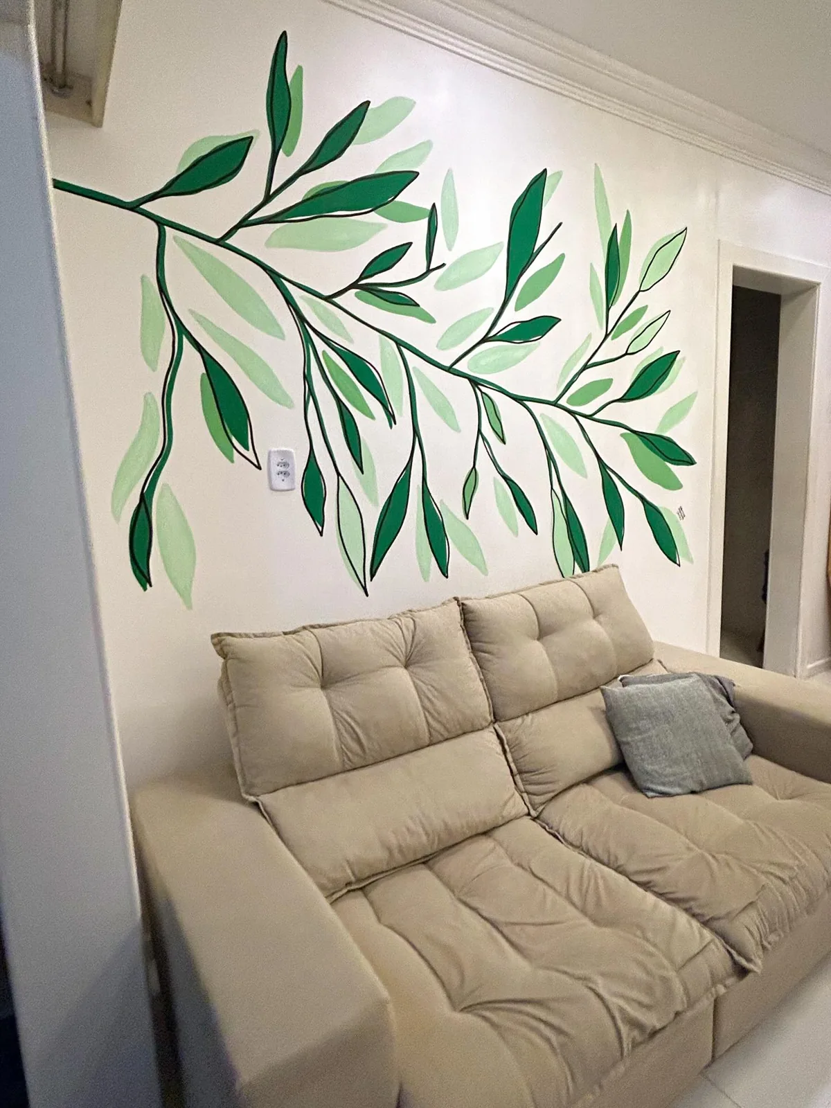 Folhagens verdes pintadas à mão na parede acima de um sofá
